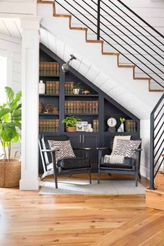 a living room filled with furniture and bookshelves next to a stair case full of books