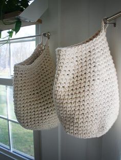 two crocheted bags hanging from hooks in front of a window