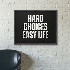 a black chair sitting in front of a white brick wall with the words hard choices easy life on it