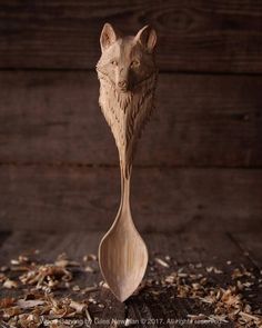 a wooden spoon with a carved animal head on it's side sitting in some wood shavings