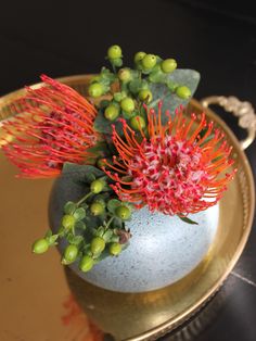 a vase with some flowers in it sitting on a table next to a gold plate