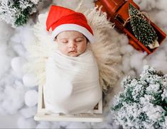 a newborn baby wearing a santa hat and sleeping on a sleigh surrounded by christmas decorations