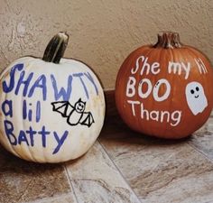 two painted pumpkins sitting side by side on the ground with words written on them