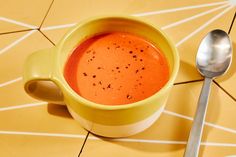 a yellow cup filled with soup next to a spoon on top of a tiled floor