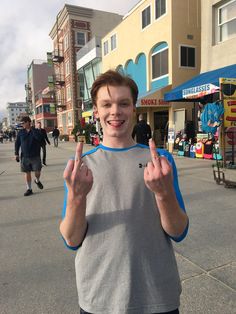 a man standing in the middle of a street making two fingers up and smiling at the camera