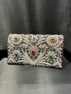 Beautiful hand-embroidered floral silk clutch bag inlaid with semi-precious stones. The front is completely covered in the design and has a closure flap with magnettic snap fastening. This clutch is perfect for daytime or night time. It is the ideal size for fitting all your essentials. It is a stylish accessory for each & every occasion. This equisite piece is even ideal for gifting to your near & dear one's . Thread - Silk Fabric - Velvet Variety of Semi-precious stones are used in this piece Zardozi is a type of heavy and elaborate metal embroidery on silk, satin, or velvet fabric base. Designs are often created using gold and silver wires and can incorporate pearls, beads, and precious stones. The embroidered silk clutch bag is made in Agra, India & is fully handmade. Designed to compl Traditional Embellished Clutch For Festivals, Elegant Embellished Embroidered Fabric For Festivals, Traditional Embellished Evening Bag For Festivals, Traditional Embellished Evening Bag For Festive Occasions, Formal Embroidered Clutch For Festivals, Festive Multicolor Embroidered Handwork Clutch, Traditional Multicolor Embroidered Clutch For Evening, Traditional Multicolor Embroidery Clutch For Evening, Traditional Evening Clutch With Intricate Embroidery