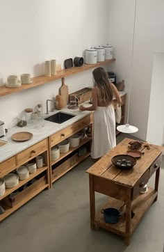 a woman standing in a kitchen next to a table with bowls and plates on it