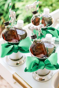 three bottles of liquor are sitting in silver cups with green bows on the top and one bottle is empty