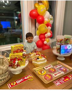 a young boy sitting at a table in front of some birthday cakes and candys