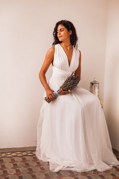 a woman in a white dress is sitting on a chair holding a bouquet and posing for the camera