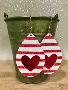 pair of red and white striped heart shaped leather earrings with gold tone hooks on top of a green bucket