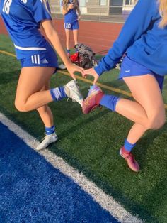 two girls in blue uniforms holding hands on a soccer field