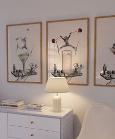 two framed pictures hang on the wall above a dresser with a lamp in front of it