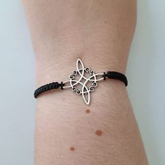 a person's arm wearing a bracelet with an intricate design on the clasp and black cord