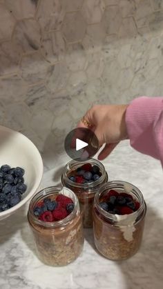 a woman is spooning blueberries and raspberries into jars on the counter