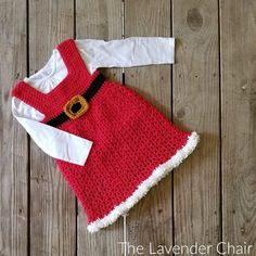 a red and white crocheted dress with a santa clause on the chest, sitting on a wooden floor