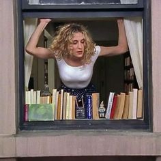 a woman standing in front of a window with books on the windowsill and holding her hands behind her head