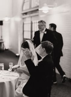 a bride and groom sitting at a table with wine glasses in front of their faces