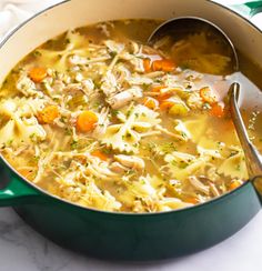 a green pot filled with chicken noodle soup on top of a white countertop