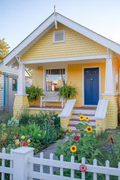 a yellow house with white picket fence and flowers