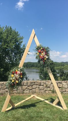 a wooden frame with flowers and greenery on it sitting in the grass next to a body of water