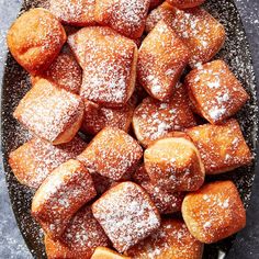 powdered sugar covered pastries are on a black platter with a spoon in it