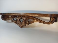 an old wooden shelf with carved designs on the top and bottom, against a white wall