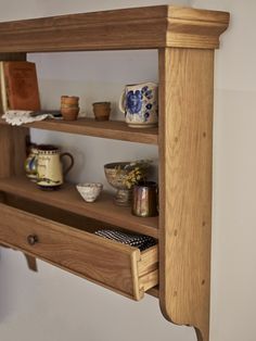 a wooden shelf with bowls and cups on it's shelves next to a wall