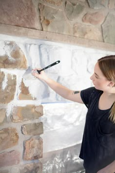 a woman is painting a brick wall with white paint on it and she has a brush in her hand