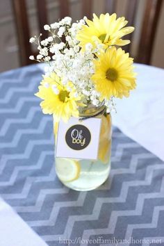 a vase filled with yellow and white flowers on top of a blue tablecloth covered table