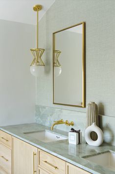 a bathroom vanity with marble counter top and gold accents on the mirror, along with two hanging lights