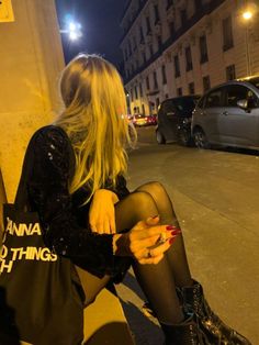 a woman sitting on the curb with her cell phone in her hand and wearing black tights