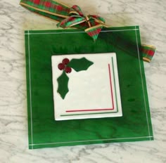 an ornament with holly on it is hanging from a green ribbon and sits on a marble surface