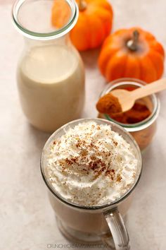 there is a cup of coffee with whipped cream in it next to some pumpkins