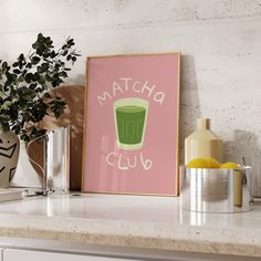 a framed poster with the words matcha club on it next to a potted plant