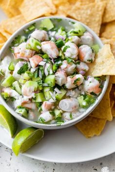 a white plate topped with guacamole and tortilla chips next to a lime