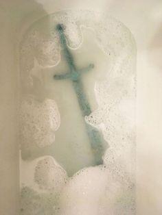 a cross is in the middle of some foamy water with bubbles around it and on top of a wall