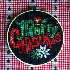 a cross stitch christmas ornament hanging on a red and white checkered tablecloth