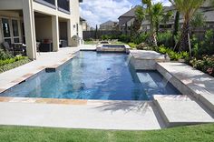 an outdoor swimming pool surrounded by lush green grass and palm trees in front of a house