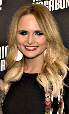 a woman with long blonde hair and blue eyes smiles at the camera while standing in front of a black backdrop