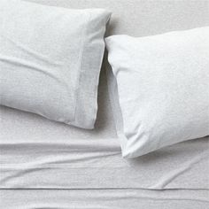 two white pillows sitting next to each other on top of a gray bed coverlet