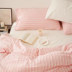 an open book on a bed with pink and white striped sheets, coffee cup, and lamp