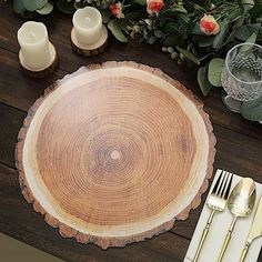 a place setting with silverware and flowers on a wooden table top in front of greenery