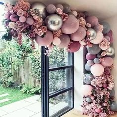 an arch made out of balloons in front of a window with a large wreath on it