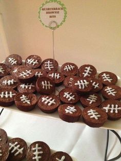 chocolate cupcakes with white frosting decorated like footballs on a table next to cookies