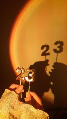 a person holding two candles with the number twenty three on them in front of a yellow background