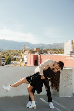 a man and woman kissing on the roof of a building with mountains in the background