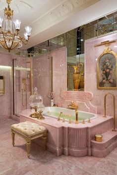 a fancy bathroom with pink marble walls and gold trimmings on the tub, chandelier, mirror, and vanity