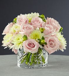 a glass vase filled with pink and white flowers on top of a table next to a gray wall