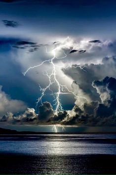 a large cloud filled with lots of lightning in the sky next to some water and clouds